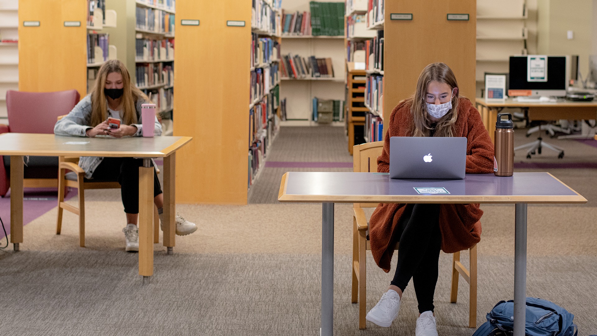 2 students wearing masks while socially distancing in the library