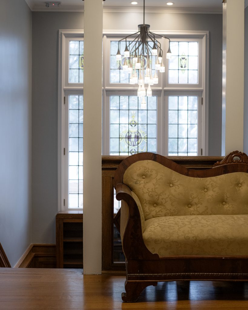 chair with the stairs, a large window, and a chandelier behind it