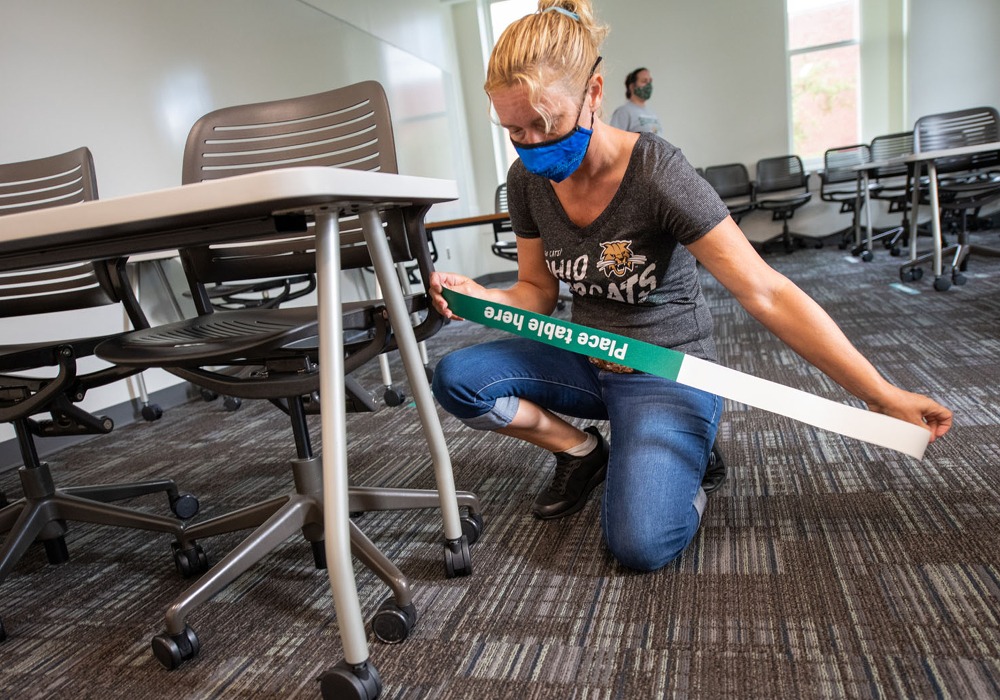 Women taping the floor to signal social distancing in the classroom