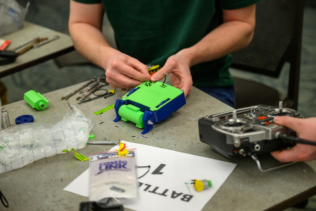 Image of a person's hands manipulating a small green and blue box-shaped robot