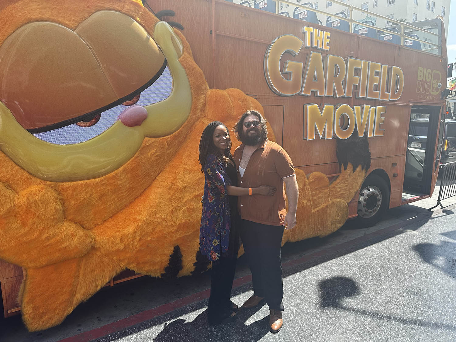a man and woman pose in front of a Garfield-branded tour bus