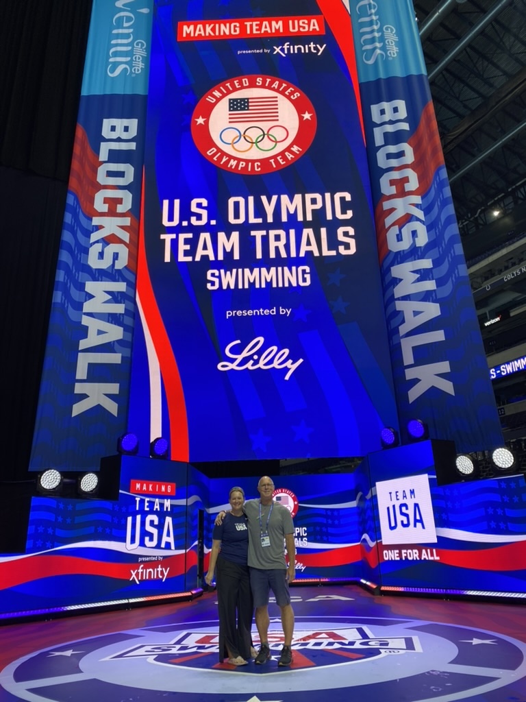 Lisa Milne poses with John Moffet, a 1984 swimming Olympian, in front of a large banner for the US Olympic Team Trials
