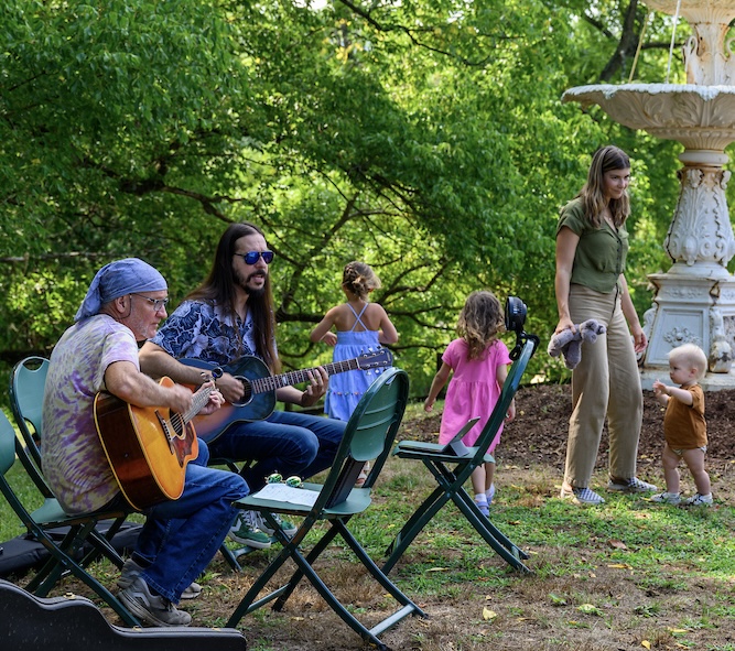 Two musicians play their instruments while kid plays in the background