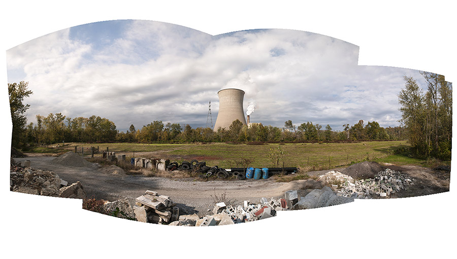 a panoramic landscape with uneven borders depicting a power plant and green field set against a cloudy sky