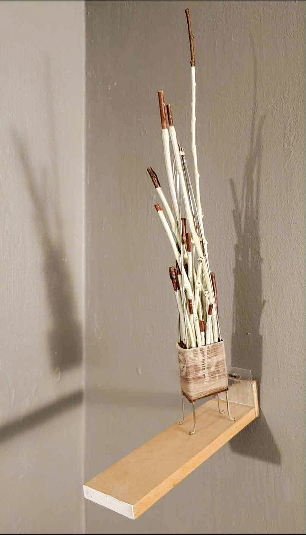 a sculptural composition of sticks painted white with brown tips on a light brown shelf