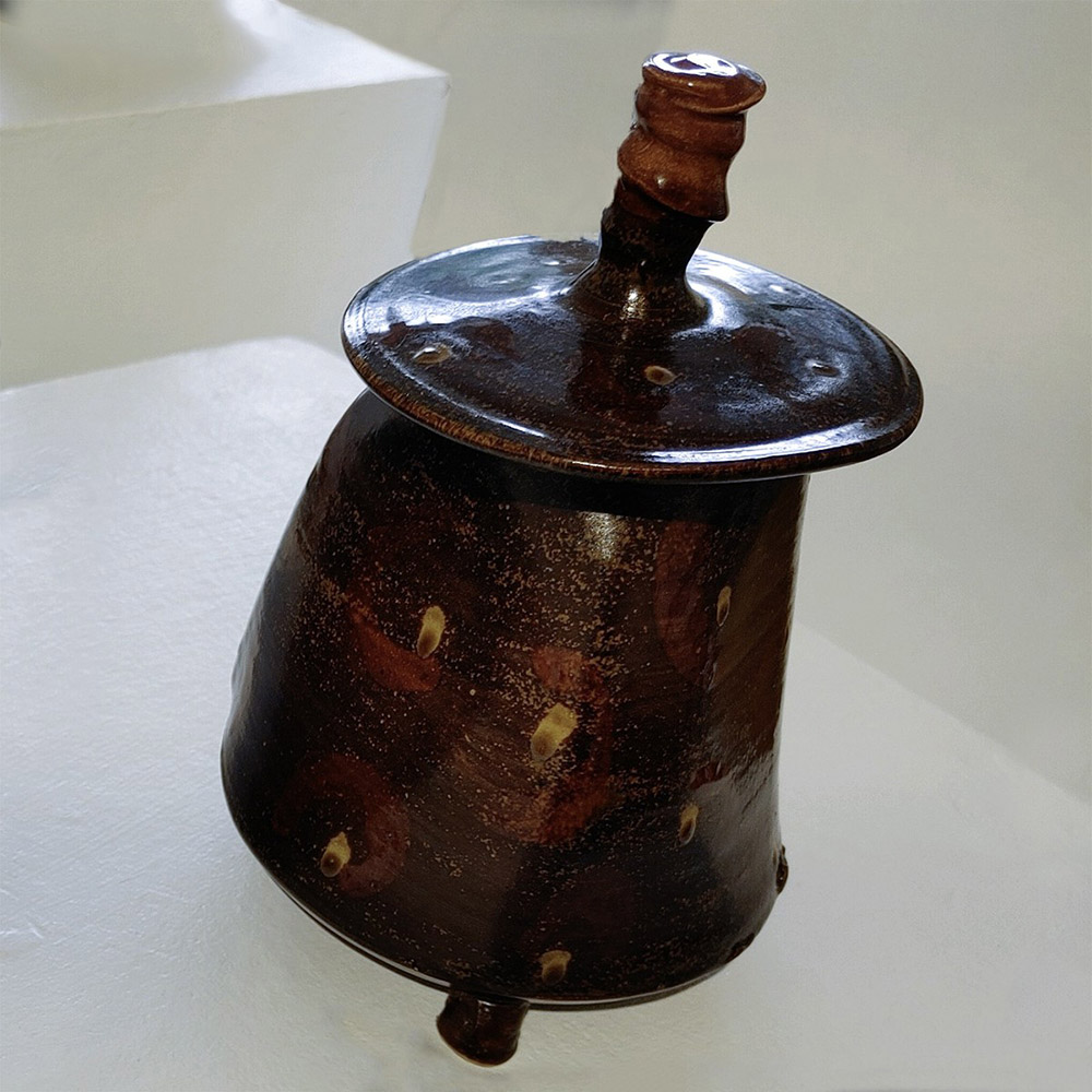 a brown ceramic jar with three feet and a lid