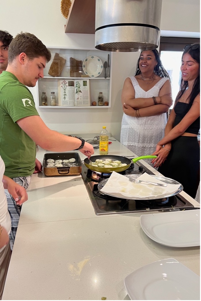 four people watch as one cooks food at the stove