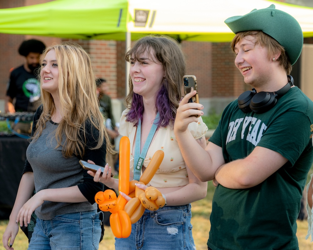 Three students stand side by side, laughing at something happening off cameraF