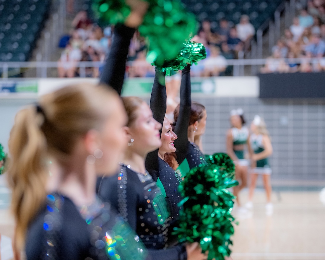 Dancers hold green pom-poms as they perform for a crowd at OHIO's Convo