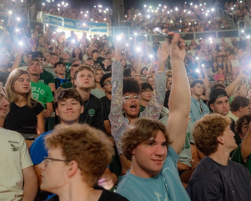 Students stand in a crowd at the Convo, raising their phone flashlights above their heads