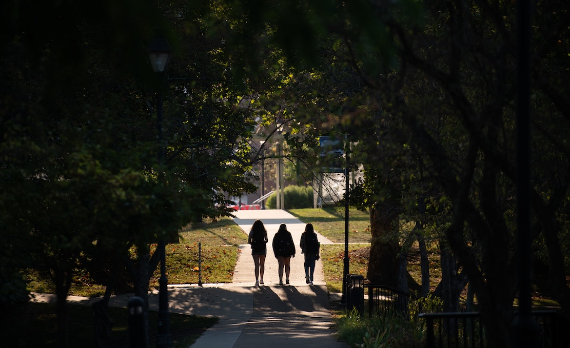 Three students pictured walking on a sidewalk in silhouette