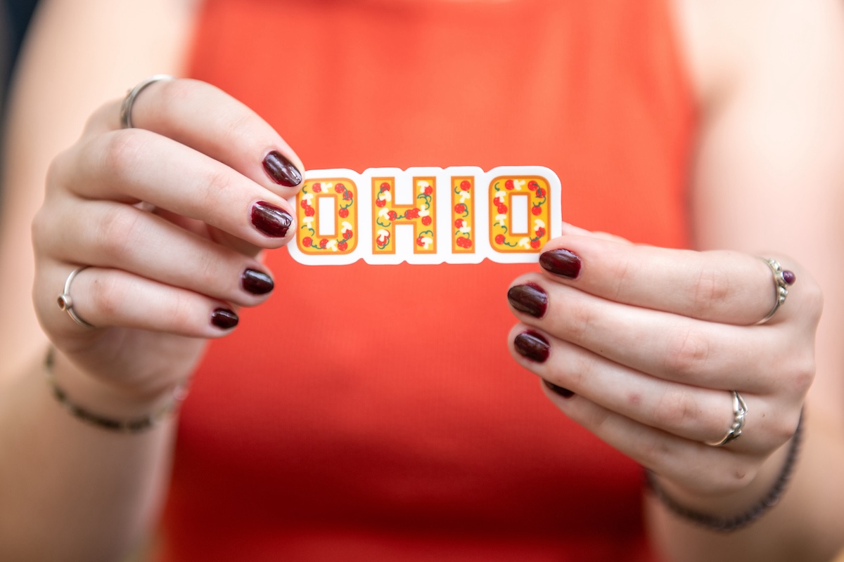 Close-up image of a person holding an OHIO sticker decorated to look like pizza