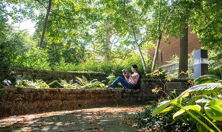 a woman in a pink shirt, jeans and glasses with short dark hair reading at Wolfe park