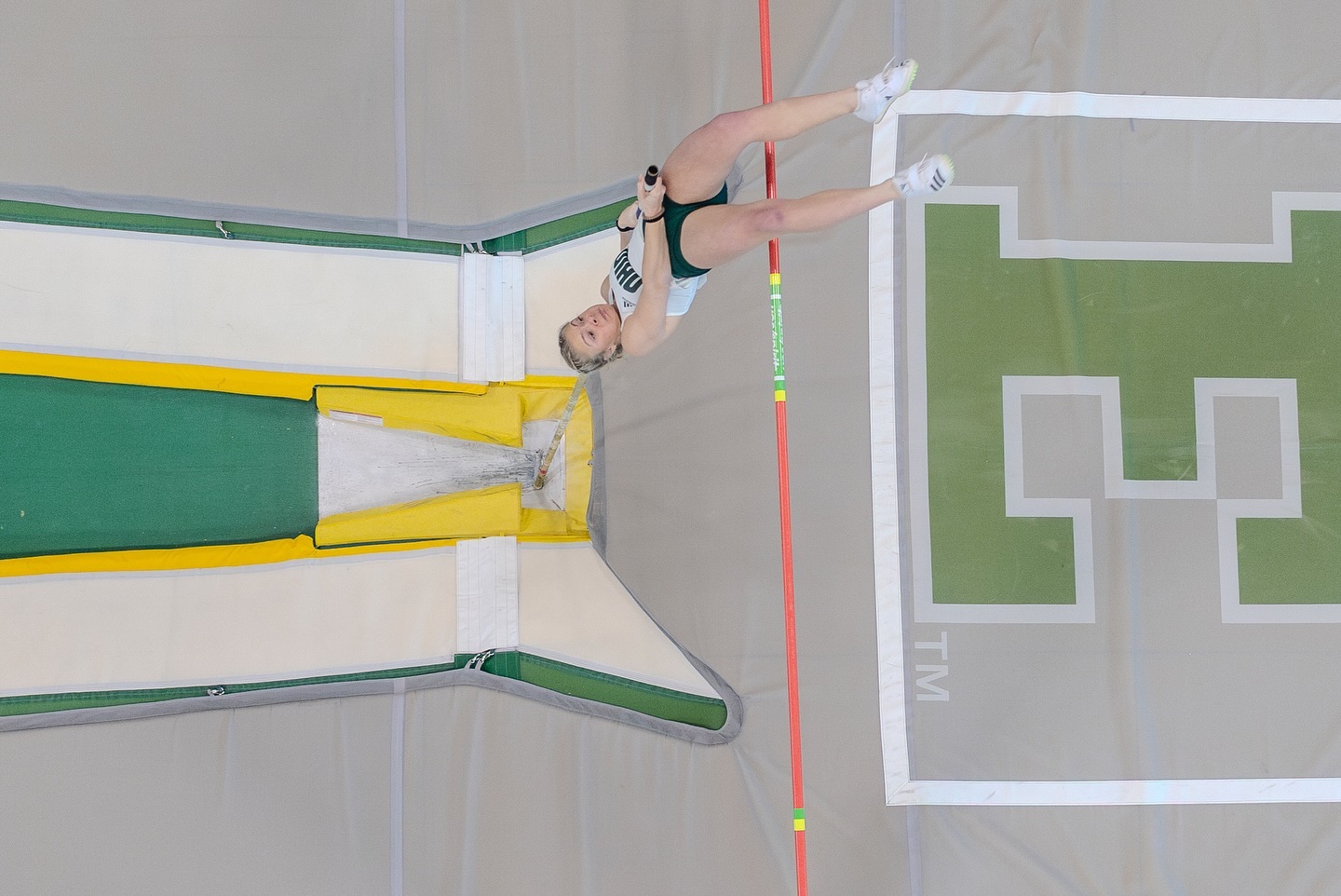 an overhead view of a female pole vaulter clearing the bar