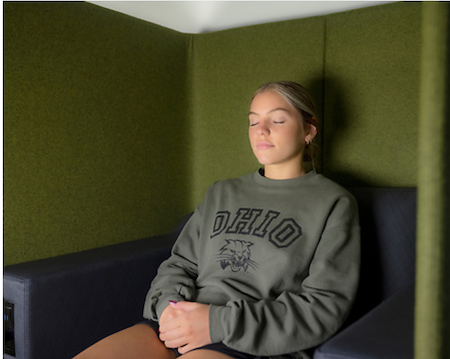 A student wearing an OHIO sweatshirt meditates with closed eyes in an enclosed, serene space 