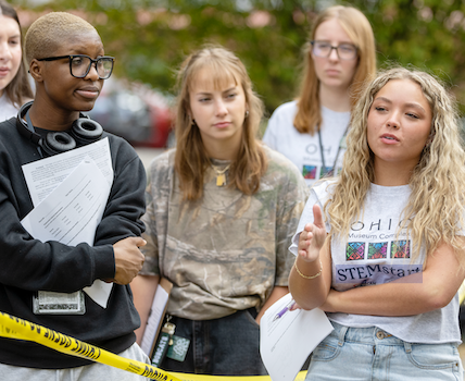 First-year science students analyze their mock crime scene activity behind "crime scene" tape