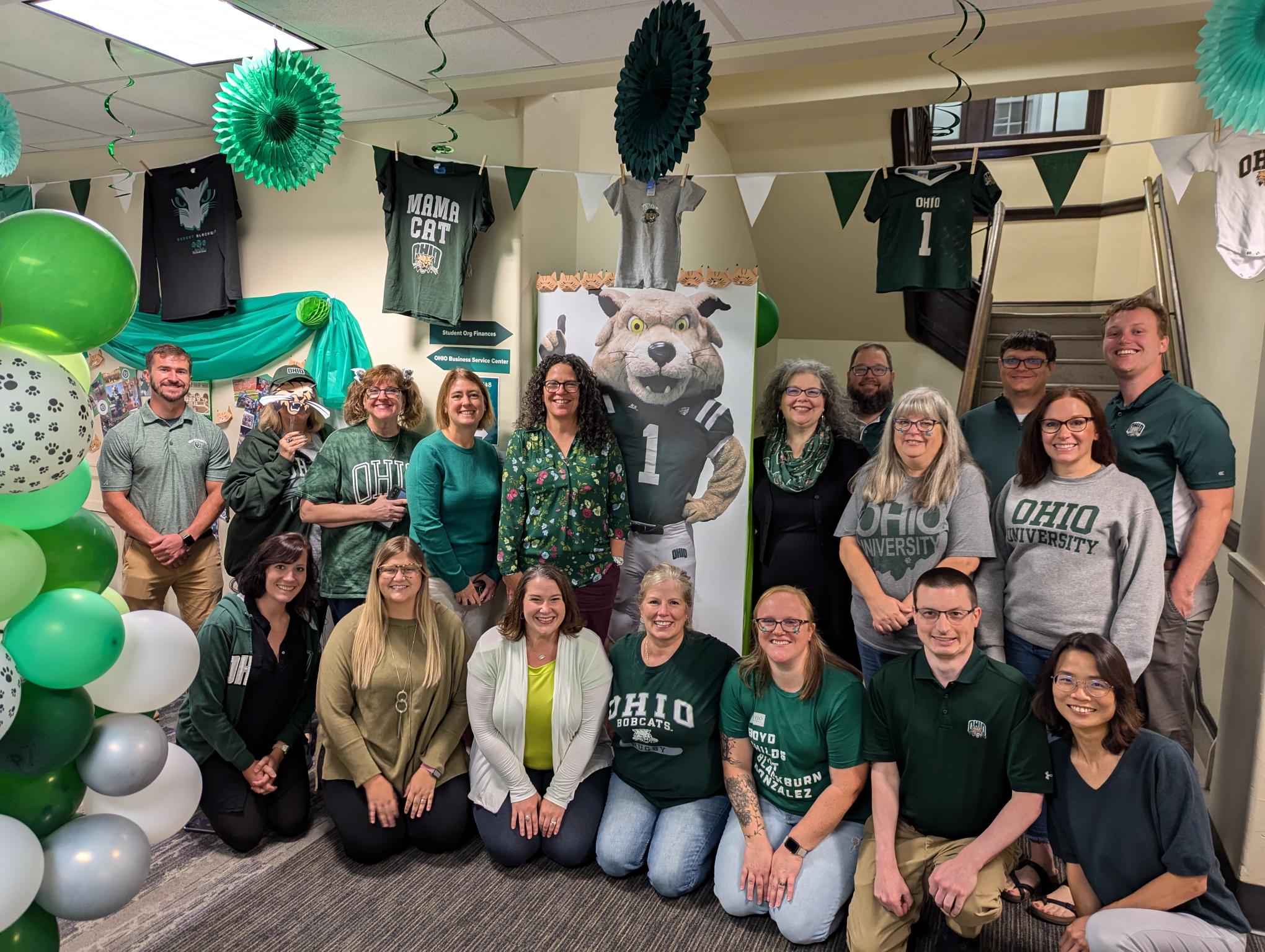 The members of the OHIO Business Service Center pose for a photo in an office decorated with green and white for Homecoming 2024