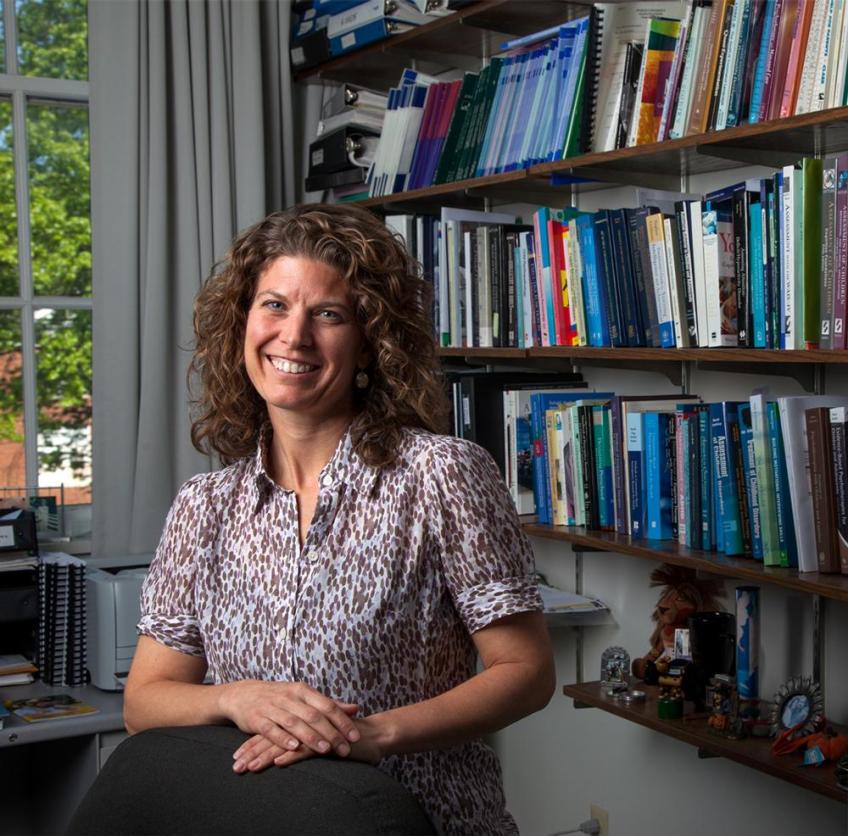 A headshot of Dr. Julie Owens smiling and standing in front of a bookcase.