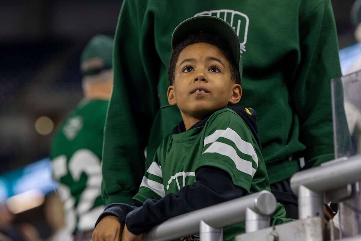 A young boy wearing a Bobcat jersey gazes past the camera at a football game