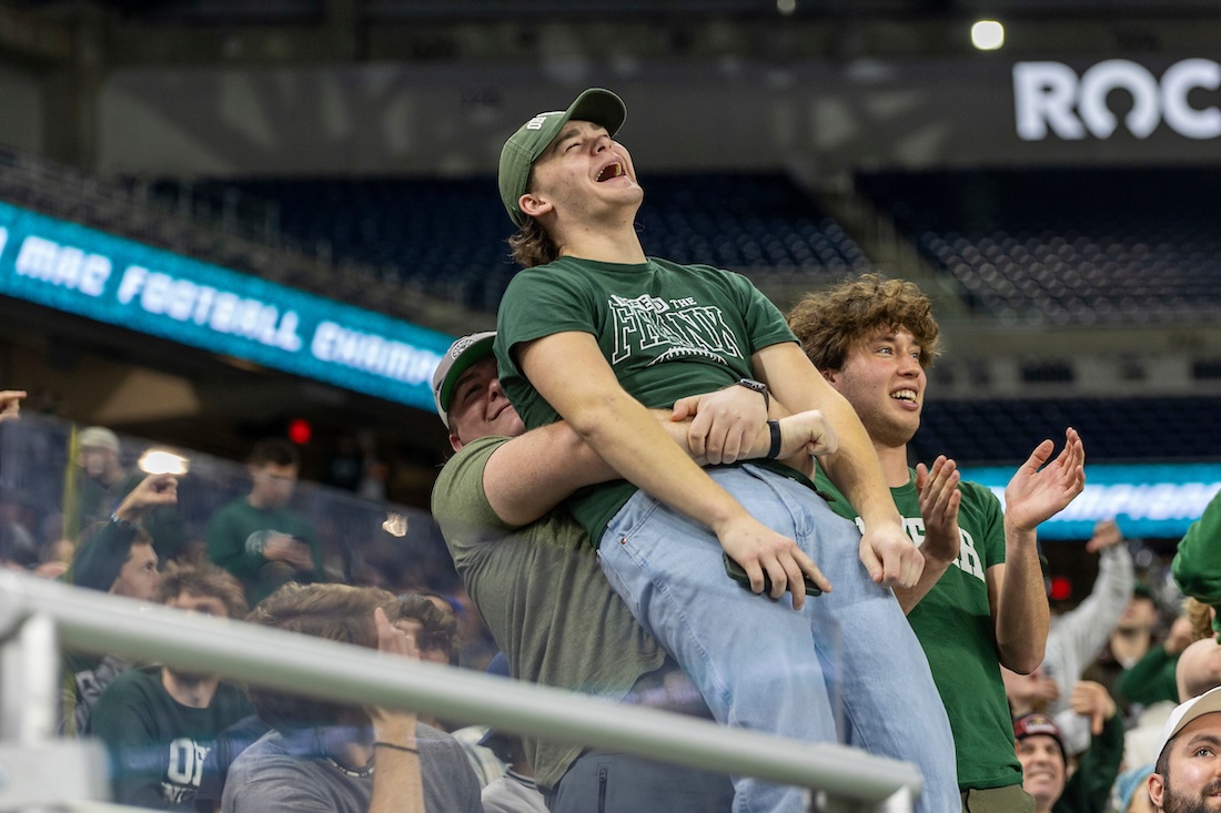 An OHIO fan smiles as his friend lifts him off the ground in the stands of the MAC championship football game