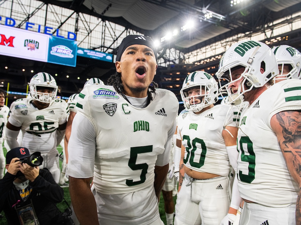 An OHIO football player stands among the team, appearing to scream in excitement