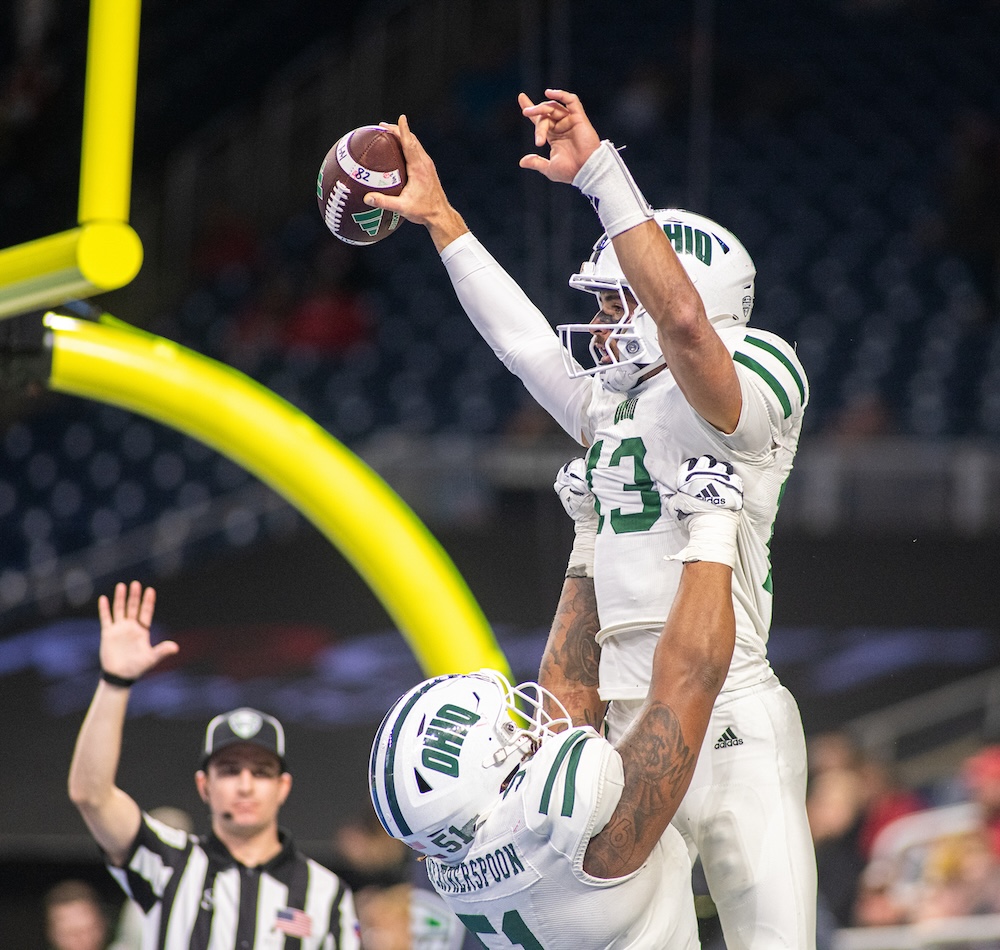 An OHIO football player lifts another in the air as a referee gestures in the background