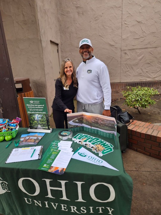 a woman and a man stand behind an ohio university branded table with marketing materials on it