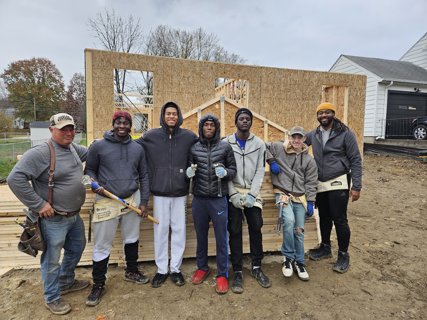 A group of men stands in front of a house mid-construction