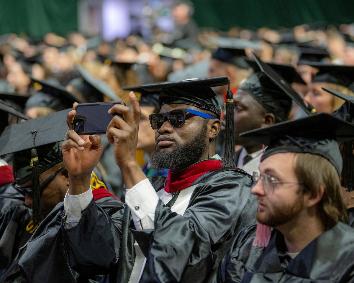 A graduate takes a photo at the Fall 2024 commencement ceremony