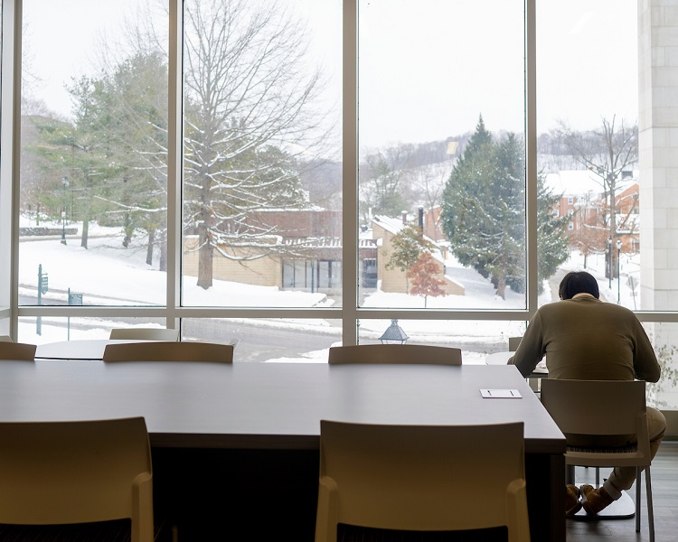 An individual studies inside an Ohio University building while snow covers the Athens Campus outside