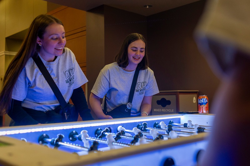 Two individuals wearing Ohio University Sibs Weekend shirts  play foosball at the GLOHIO event in Baker University Center.