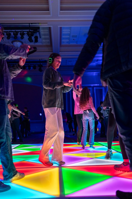 An individual dances on a lit up, colorful dance floor at the GLOHIO event