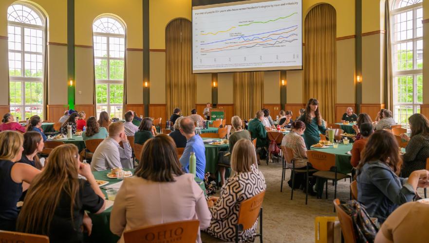 A speaker is shown talking to a large crowd of faculty and staff at the Student Success Summit in the Walter Hall Rotunda