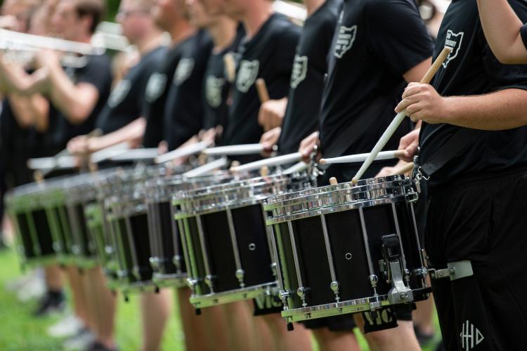 A line of marching 110 drummers stands together holding their drumsticks