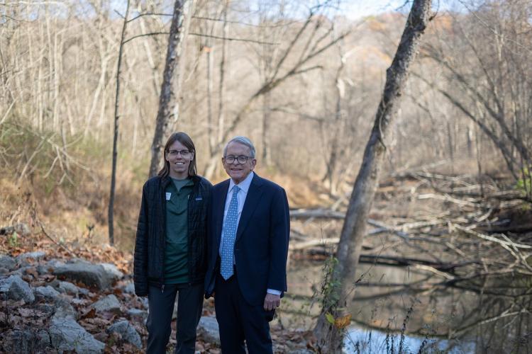 Amy Mackey and Gov. Mike DeWine are shown standing next to Raccoon Creek