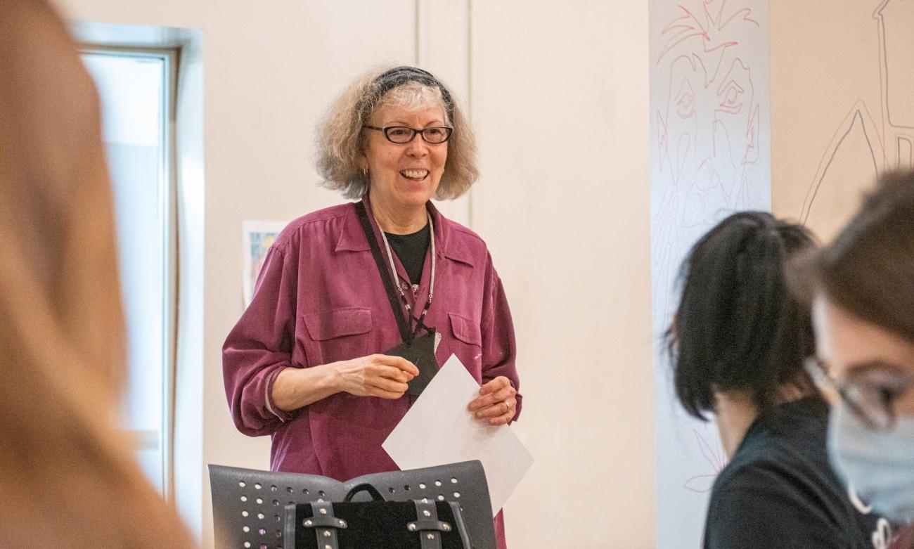 Professor Julie Elman is standing, smiling as she talks to some of her students who are looking in her direction.