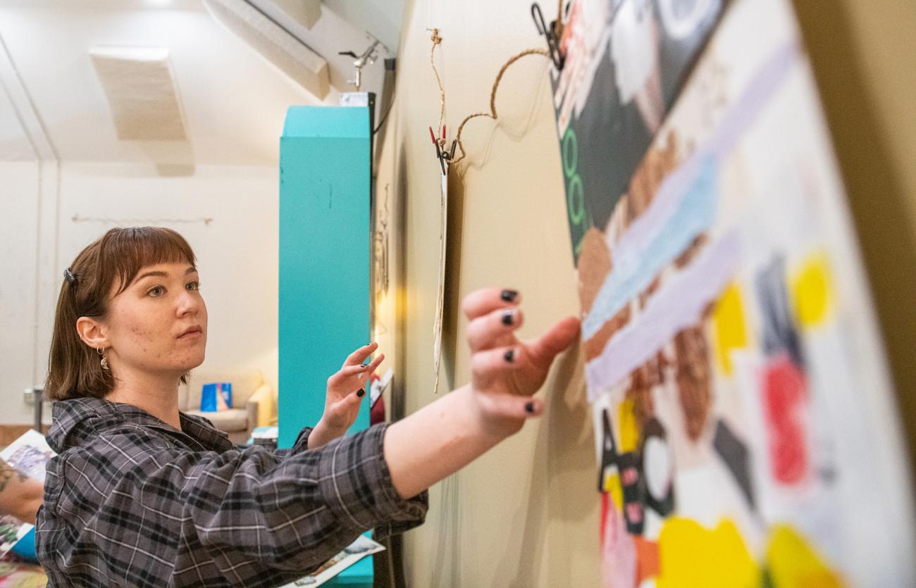 A student hangs up a collage on the wall of a classroom.