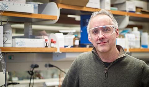 Dr. Dennis Wright wearing safety goggles in front of chemical shelves