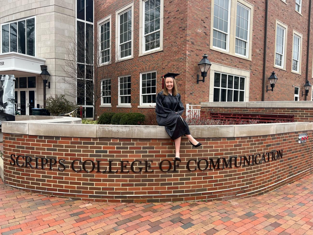 Kirsten Thomas sits on a side wall that reads 