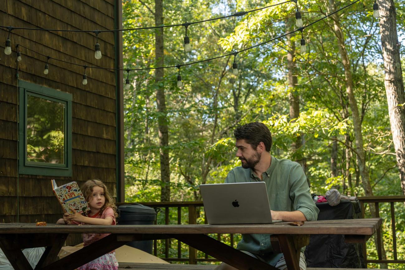 An OHIO student works on a laptop next to a child reading a book.