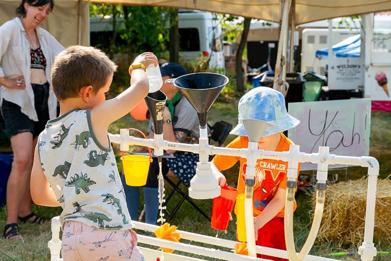 Two kids with colorful outfits play with water at the NMF Kids Area.