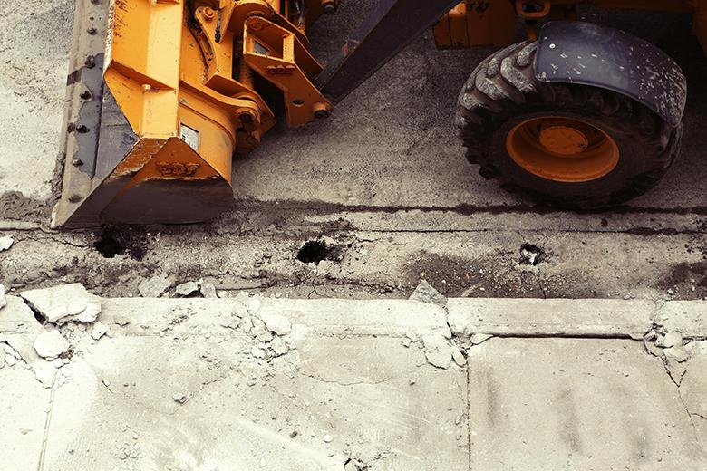 Construction equipment next to a damaged street and sidewalk.