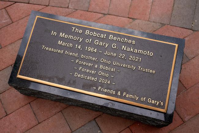 A phot of the plaque, which says - The Bobcat Benches In Memory of Gary G. Nakamoto, March 14, 1964 - June 22, 2021 - Treasured friend, brother, Ohio University Trustee, Forever a Bobcat - Forever Ohio - Dedicated 2024 - Friends and Family of Gary's