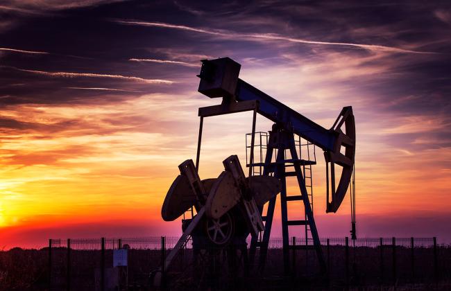 An oil derrick in front of a sunset.