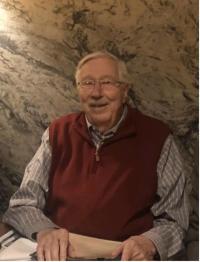 A man wearing a sweater vest smiles at the camera