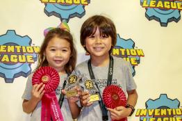 Two children pose for a photo with award ribbons