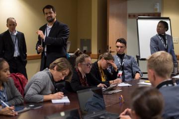 Some students sit, stand around a table during the mock foreign policy exercise.