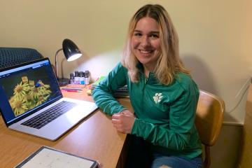 Sarah Romer smiles at the camera with a laptop on a desk to the left 