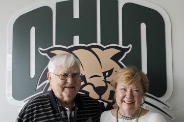 Alumni Tom and Gwen Weihe pose in front of the OHIO logo