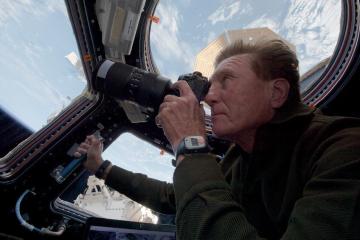 A man on a space capsule holds up a camera and takes photos of Earth from space.